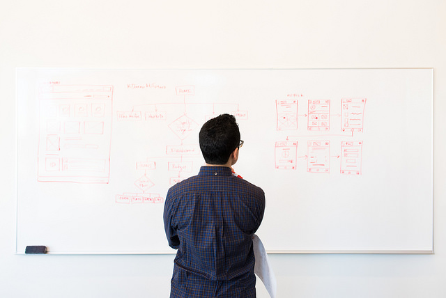 Person standing at whiteboard observing flow charts